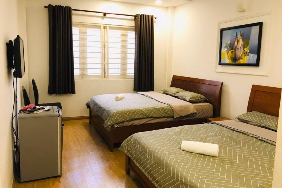 A hotel room with two beds, a small desk, and a painting on the wall.