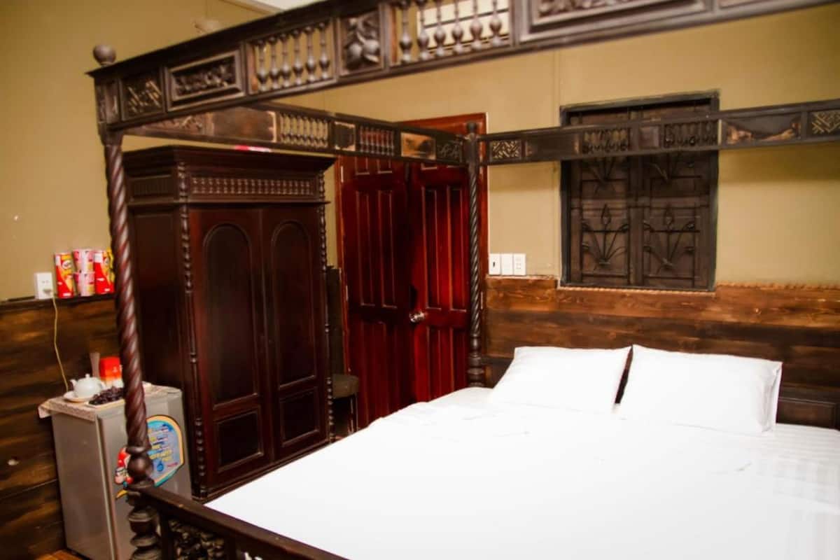 A bedroom with a wooden four-poster bed, a red door, and a window with decorative iron bars.