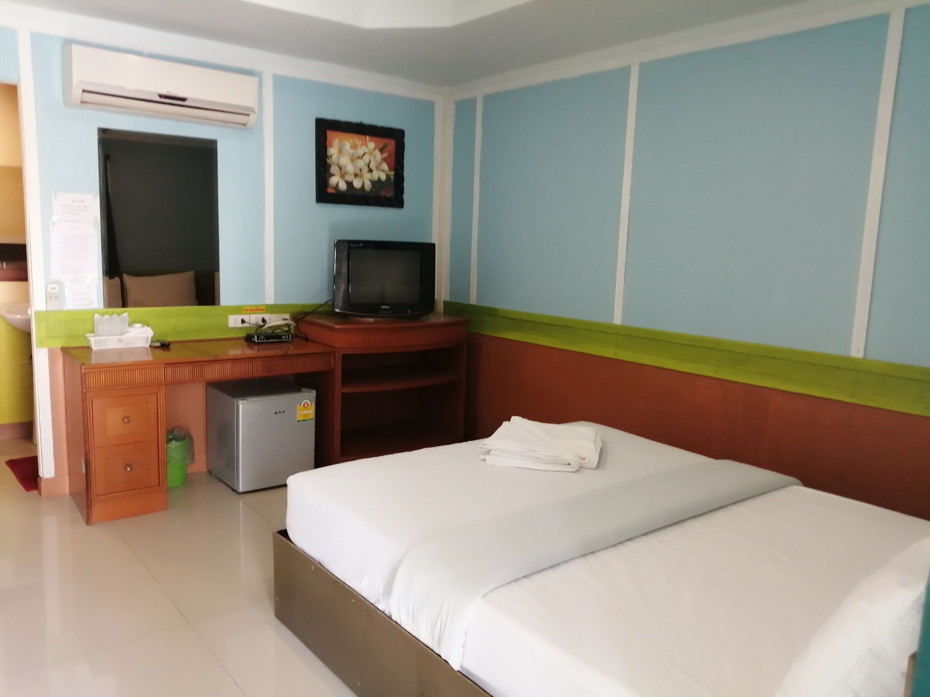 A hotel room with a bed, a desk with a television, an air conditioner, and a small refrigerator.