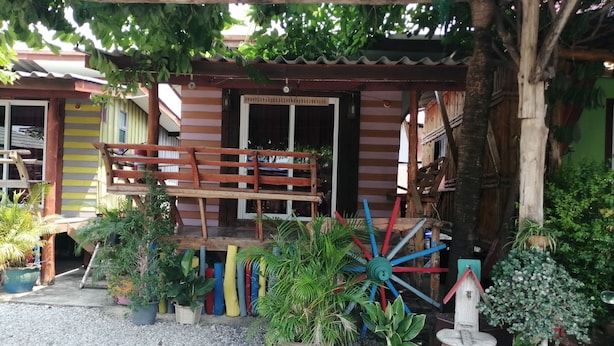 Une maison en bois rustique, dotée d’un porche et entourée de différentes plantes en pot, ainsi que d’un grand moulin à vent décoratif.