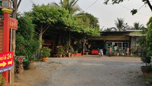 Une entrée rustique, avec un chemin de gravier menant à un espace abrité agrémenté de plantes en pot et d’un petit bâtiment sur lequel est fixée une enseigne.