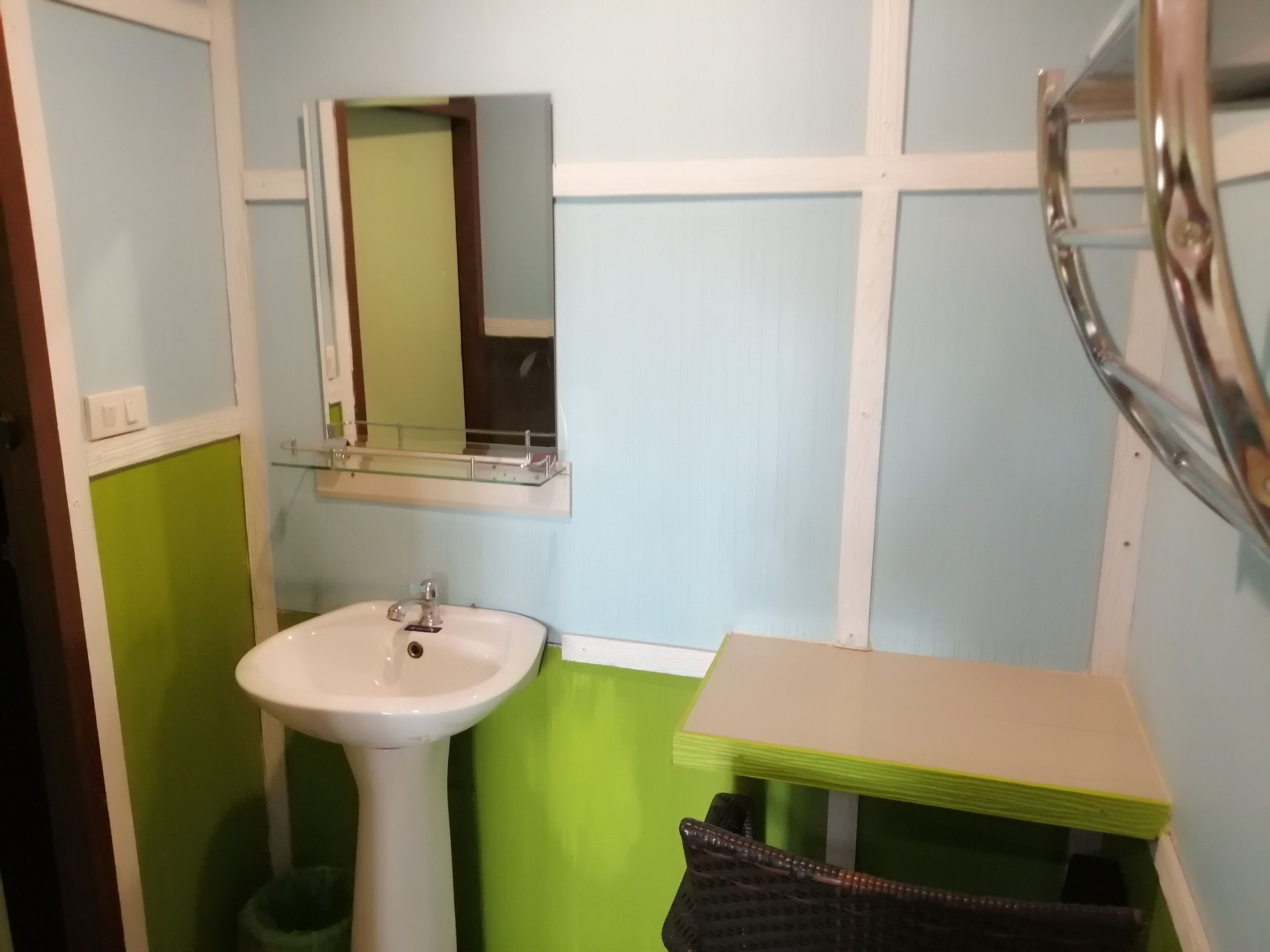 Un baño con un lavamanos blanco de pedestal, un espejo encima y un tocador pequeño verde y beige.