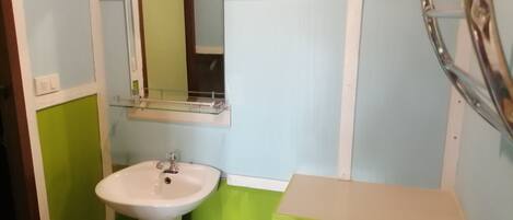 Un baño con un lavamanos blanco de pedestal, un espejo encima y un tocador pequeño verde y beige.