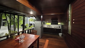 A wooden interior with a dining table, chairs, and a kitchen area with a refrigerator and sink. - Tann Anda Resort (Thep Krasattri)