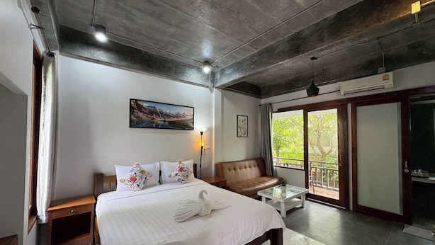 A modern hotel room with a large bed, a sofa, a glass coffee table, and a balcony with a view. - Tann Anda Resort (Thep Krasattri)