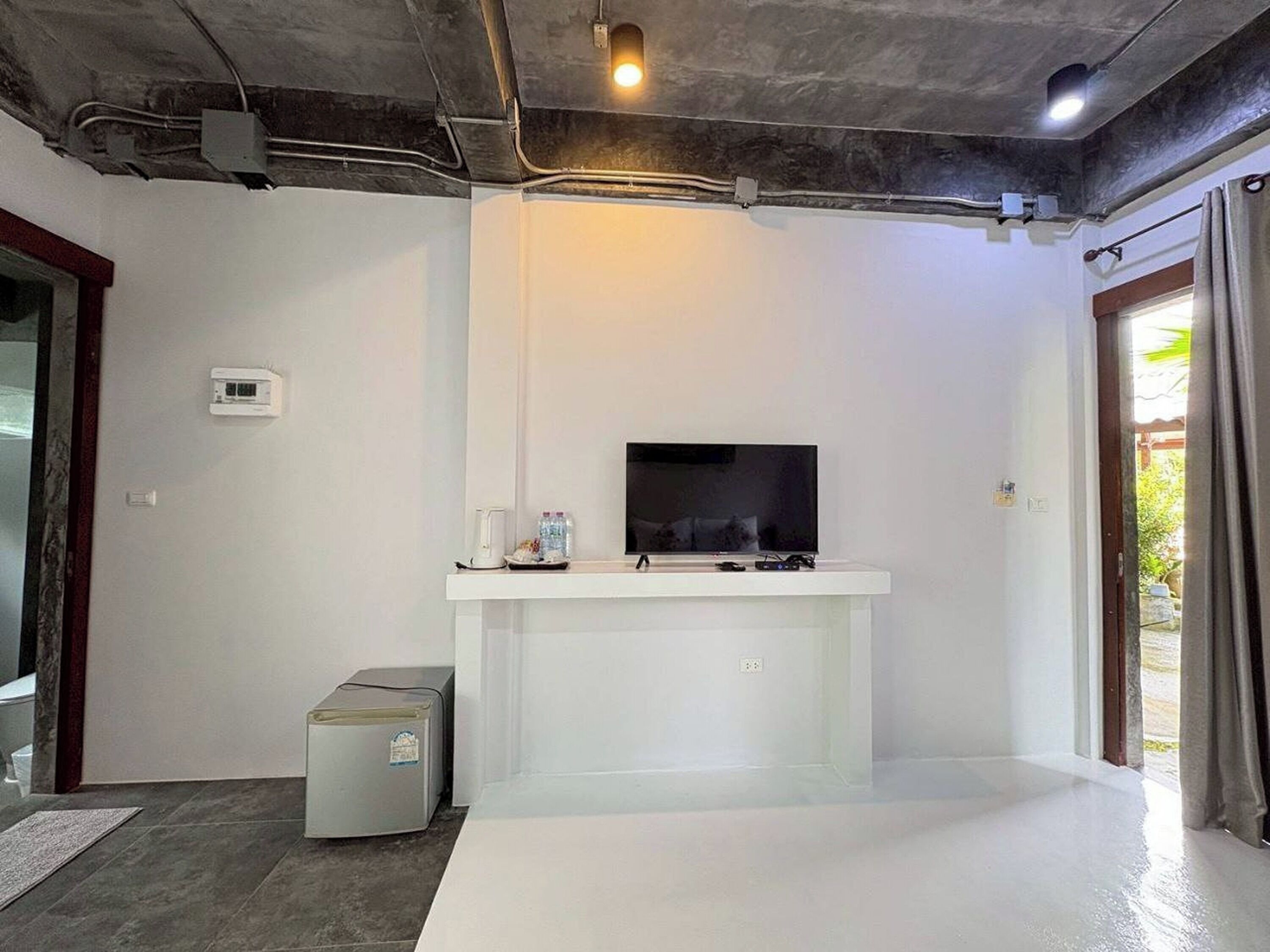 A modern living room with a flat-screen TV on a white stand, a small heater, and a water dispenser on a shelf.