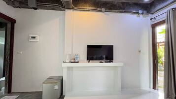 A modern living room with a flat-screen TV on a white stand, a small heater, and a water dispenser on a shelf.