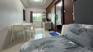 A hotel room with a sofa, a dining table with chairs, a small kitchenette, and a view of greenery outside. - Tann Anda Resort (Thep Krasattri)
