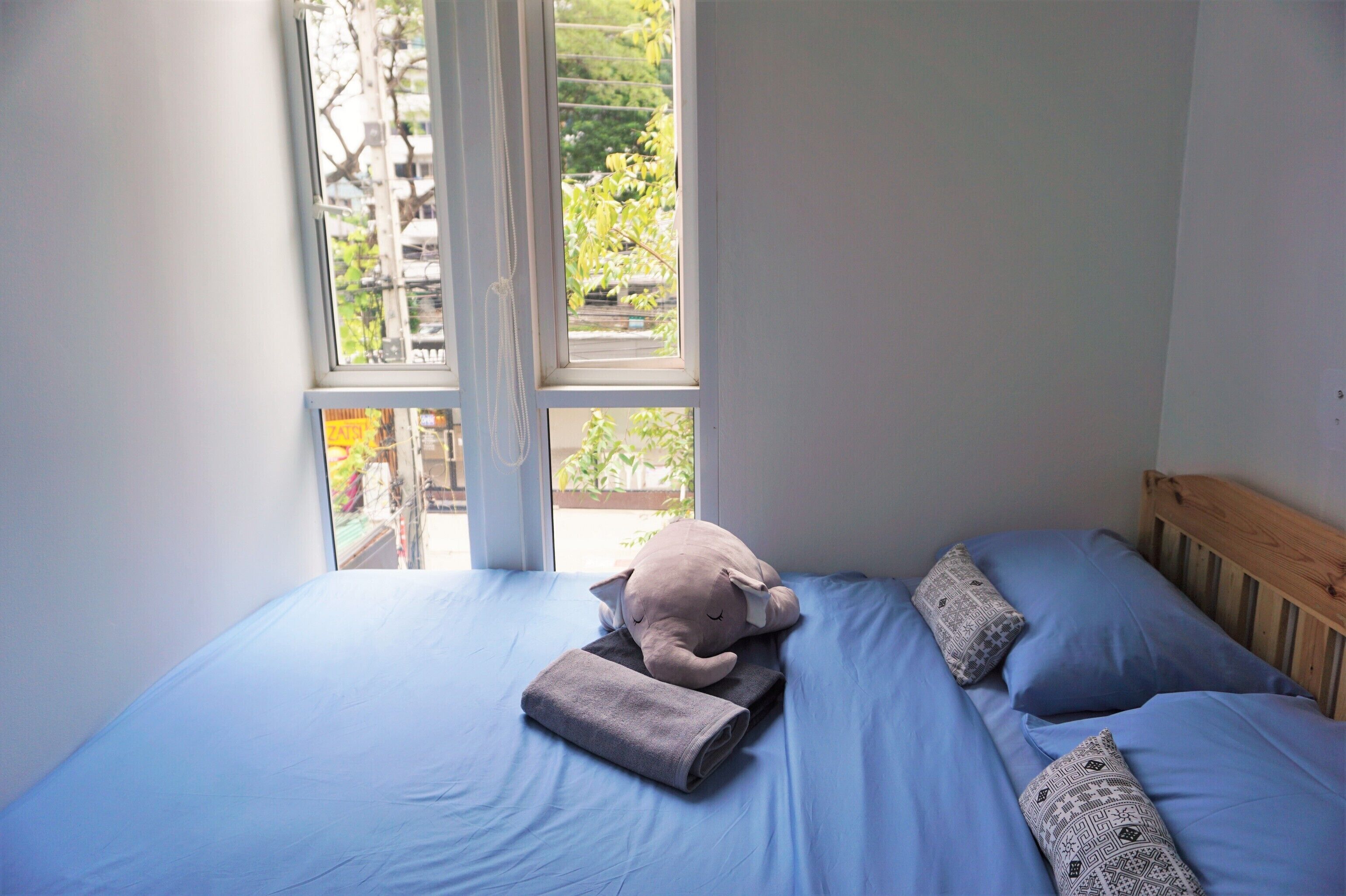 A bed with a grey blanket and pillows, a window with a view of greenery, and a wooden headboard.
