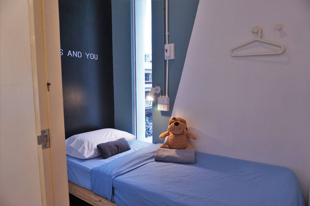 A small, neatly made bed with a blue bedspread and a plush toy on it.