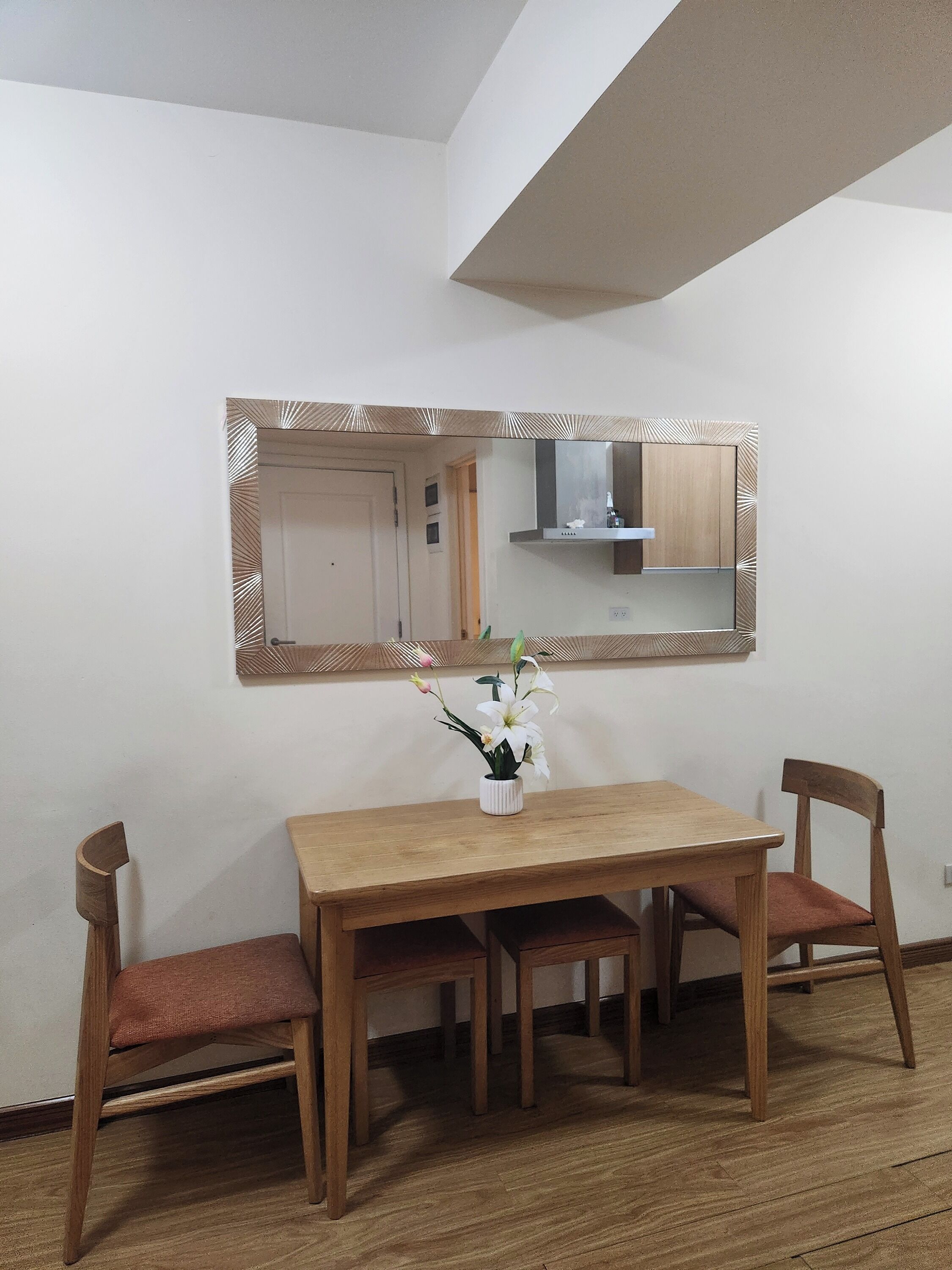Un comedor con mesa y sillas de madera, un espejo con marco decorativo y una pequeña planta en maceta sobre la mesa.