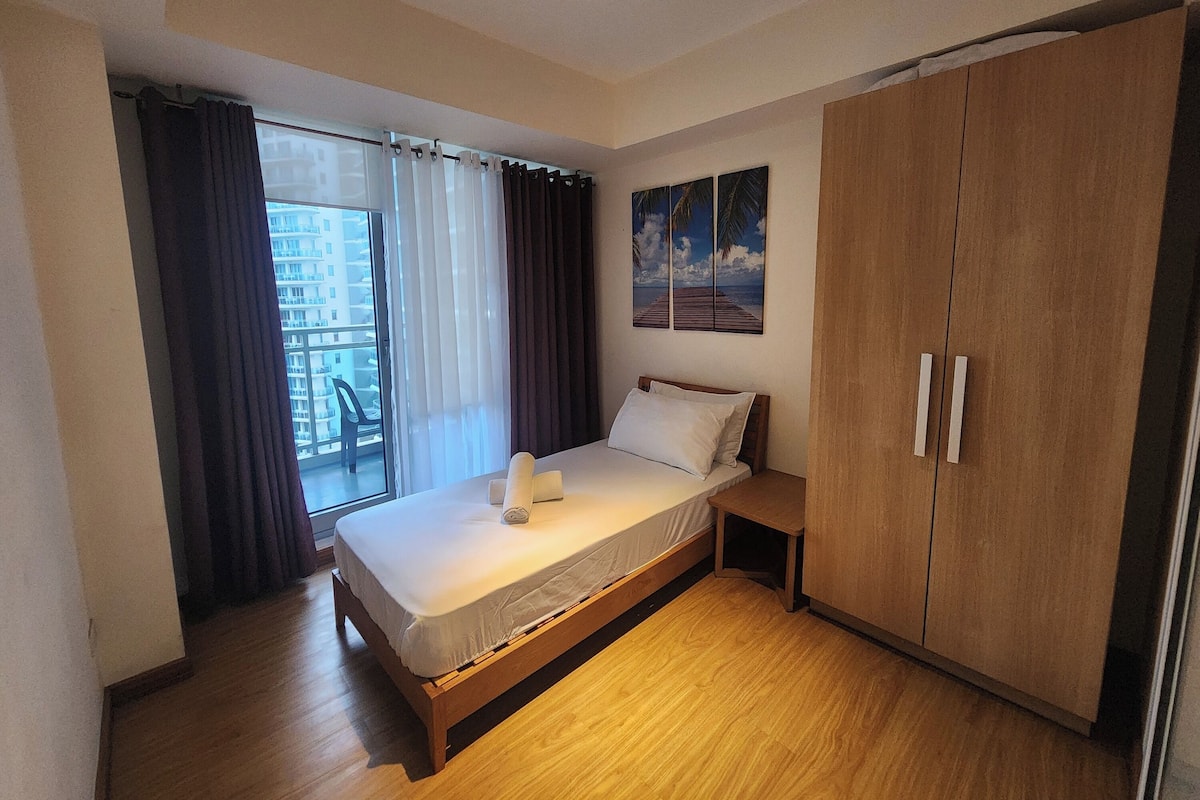 A bedroom with a wooden bed, a wardrobe, a window with curtains, and a painting on the wall.