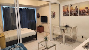 A hotel room with a bed, a sofa, a glass coffee table, a desk with a chair, and a TV. - Azure Staycation Philippines by AMRS Near Manila International Airport (Parañaque)