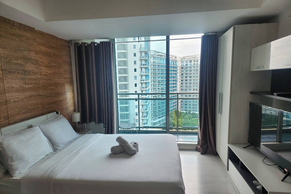 A hotel room with a large bed, a TV, and a view of high-rise buildings.