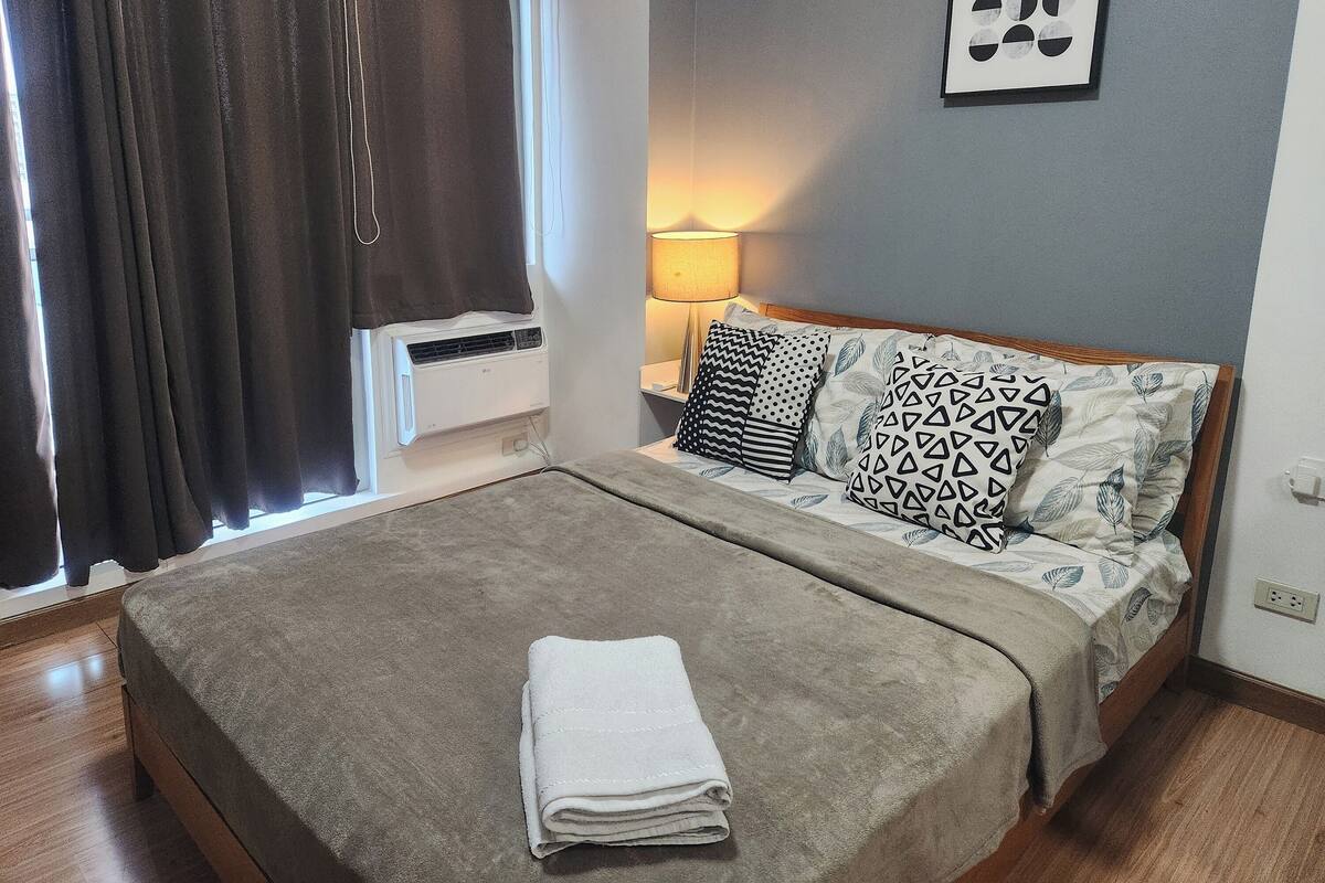 A neatly made bed with a folded towel, a bedside lamp, and patterned pillows.