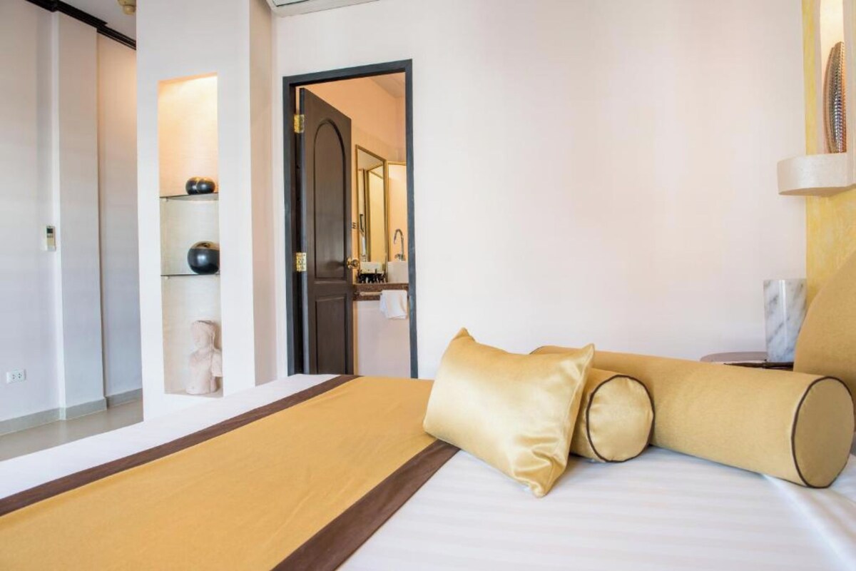 A hotel room with a bed, a mirror, a shelf with decorative items, and a door leading to another room.