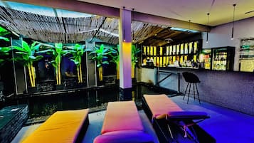 A modern indoor pool area with lounge chairs and a bar.