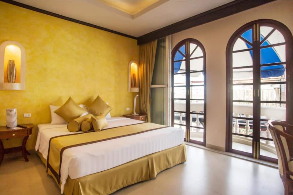 Une chambre d’hôtel avec un grand lit, deux tables de chevet et une vue sur l’extérieur grâce à des fenêtres en arc de cercle.