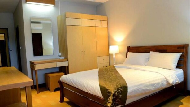 A hotel room with a wooden bed, a desk, a chair, a wardrobe, and a mirror. - My Living Place Samui (Koh Samui)
