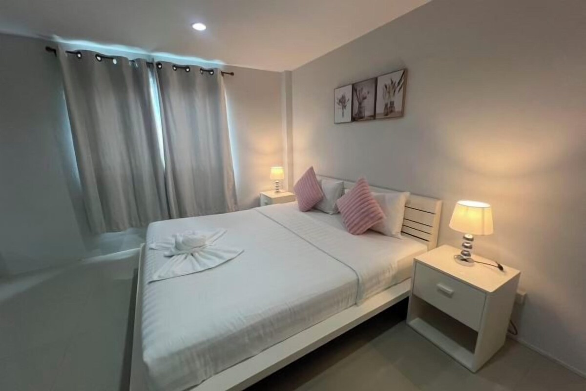 Una habitación de hotel con cama, mesitas de noche, lámpara, cortinas y cuadros en la pared.