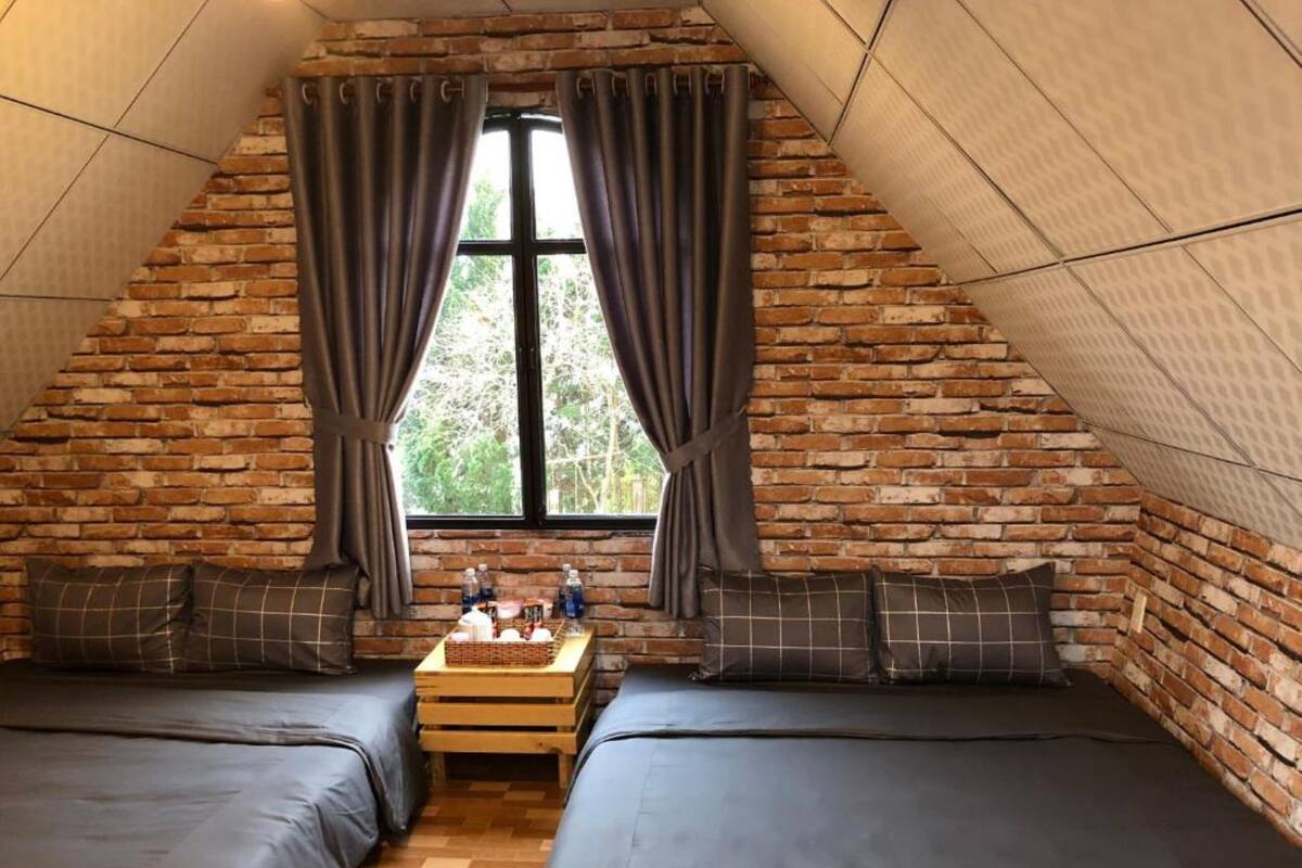 A cozy attic bedroom with two beds, a wooden table, and a window with curtains.