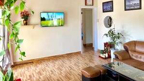 A living room with a wooden floor, a brown leather sofa, a TV on the wall, and a plant. - Pine Tree House Da Lat (Lam Vien - Da Lat)