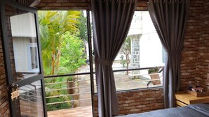 A bedroom with a large window, a bed, a wooden floor, and a brick wall. - Pine Tree House Da Lat (Lam Vien - Da Lat)