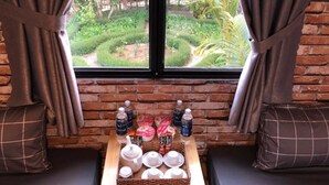 A room with a brick wall, a window with curtains, a tray table with tea sets, and a view of a garden. - Pine Tree House Da Lat (Lam Vien - Da Lat)