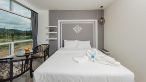 A hotel room with a large window, a bed with white linens, a decorative wall piece, and a small table with a vase of flowers. - Vacation Time House (Sa Khu)