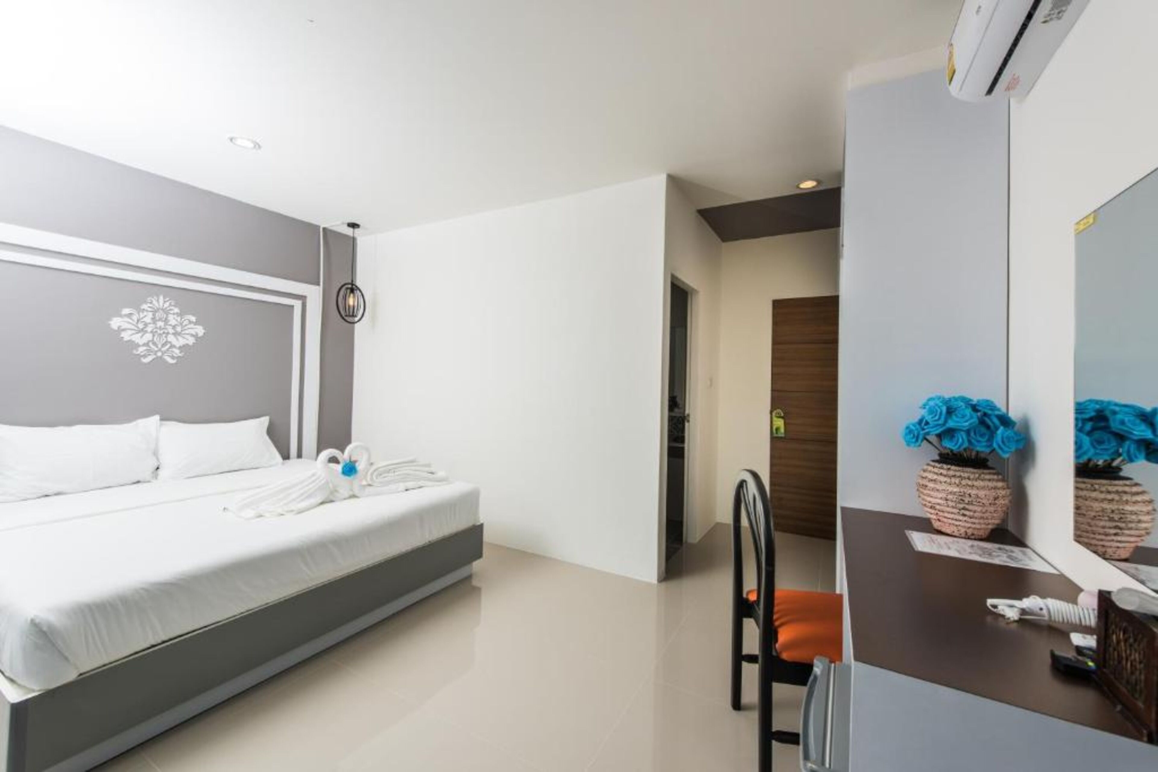 A modern hotel room with a large bed, a desk with a mirror, and a vase of flowers.