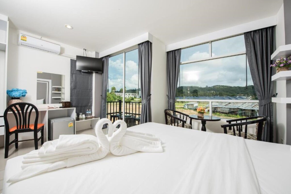 A hotel room with a bed, a desk, a chair, a TV, and a balcony with a view.
