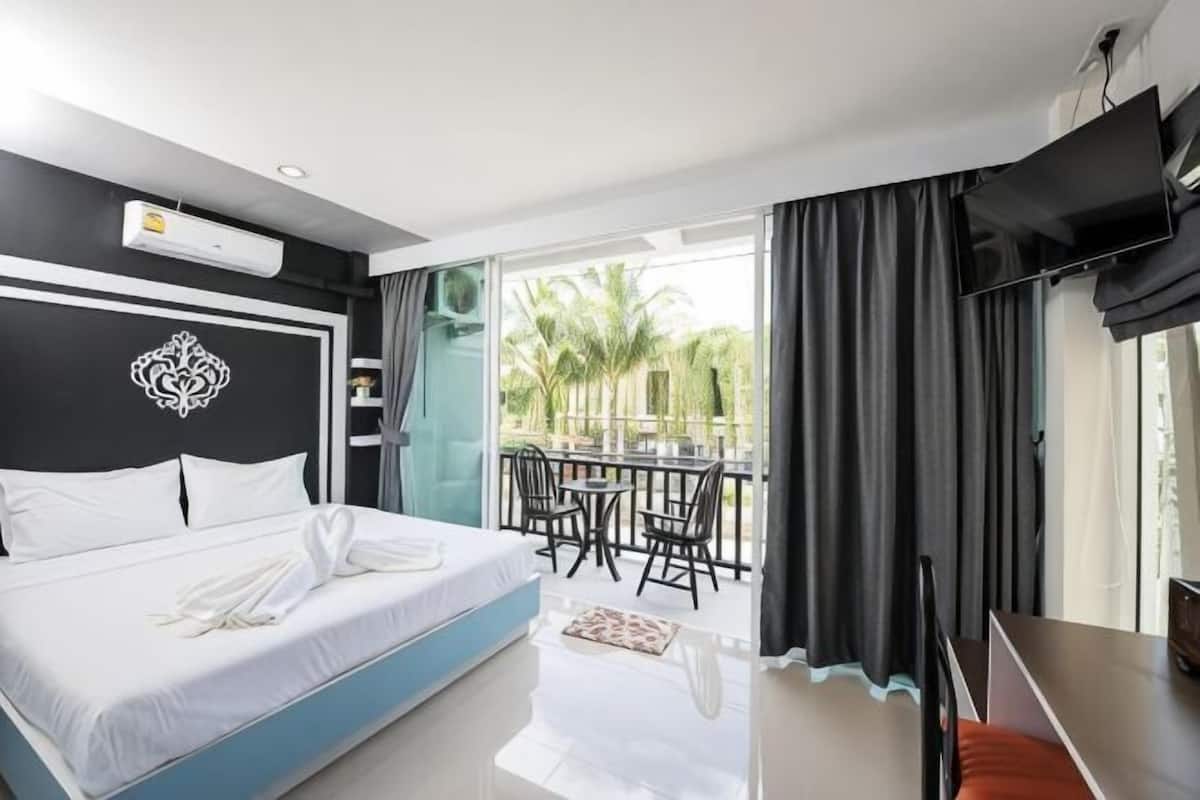 A hotel room with a bed, a desk, a TV, and a balcony with chairs.