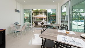 A modern dining area with glass walls, a view of the outdoor garden, and a variety of seating arrangements. - Vacation Time House (Sa Khu)