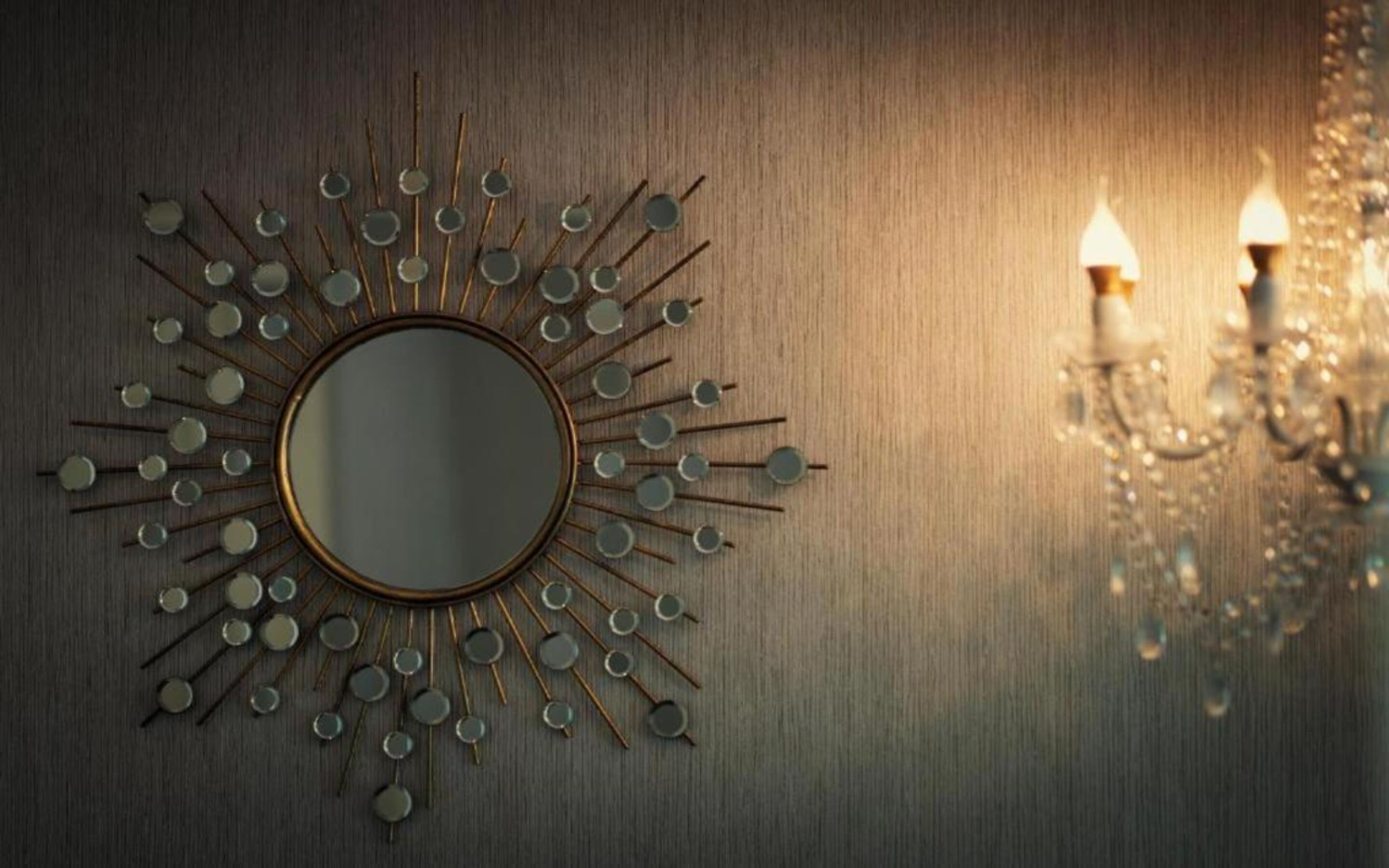 A wall-mounted mirror with a sunburst design, two wall sconces, and a chandelier reflection.