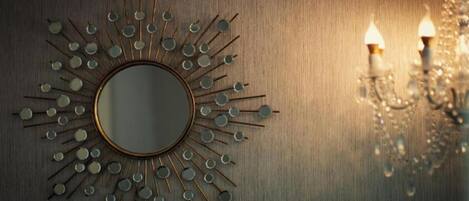Espejo empotrado con diseño de sol, dos apliques de pared y el reflejo de una araña.