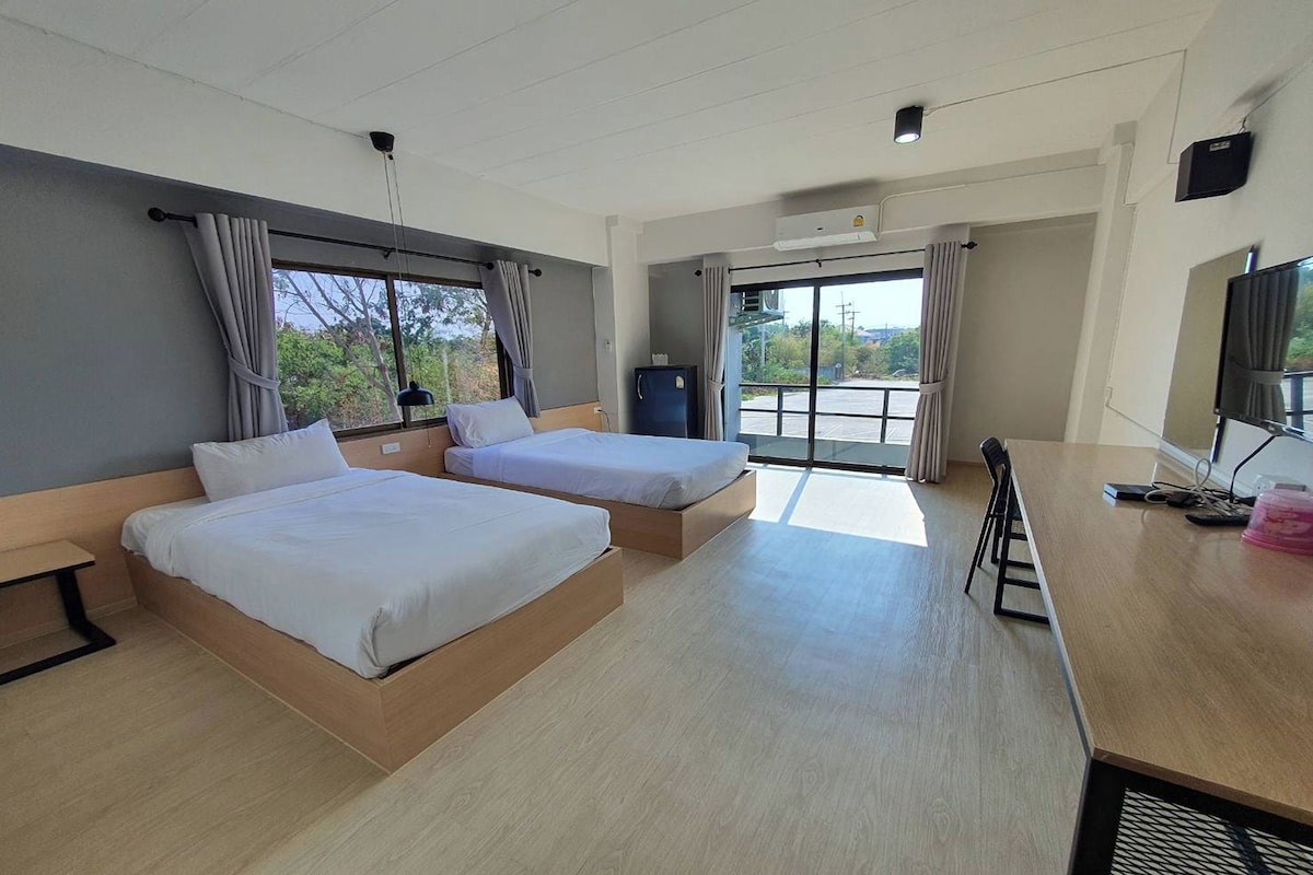 A hotel room with two beds, a desk, a television, and a view of the outdoors.
