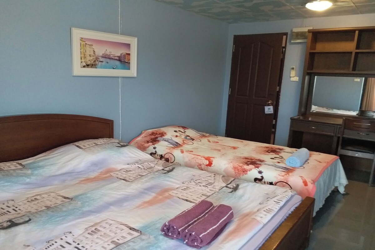 A bedroom with a bed, a wooden headboard, a wall-mounted picture, a door, and a desk with a mirror.