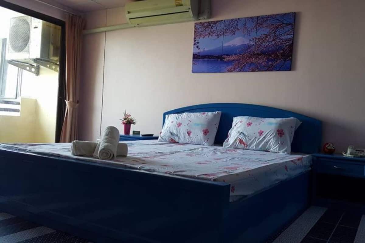Ein Schlafzimmer mit Bett, Kissen, einem Nachttisch, einer Wand-Klimaanlage, einem Fenster und einem Gemälde.