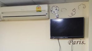 A room with a refrigerator, an air conditioner, a flat-screen TV mounted on the wall, and a wall socket.