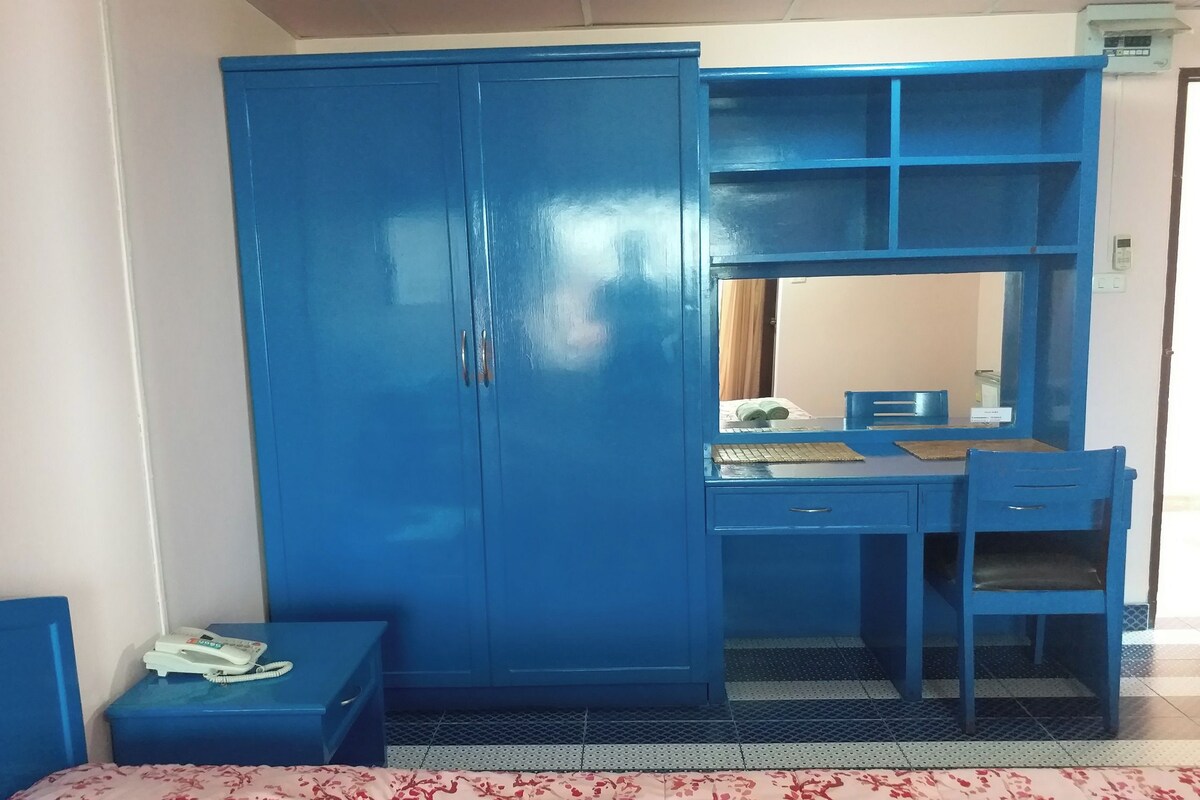 A room with a blue wardrobe, a desk with a chair, and a telephone on a small table.