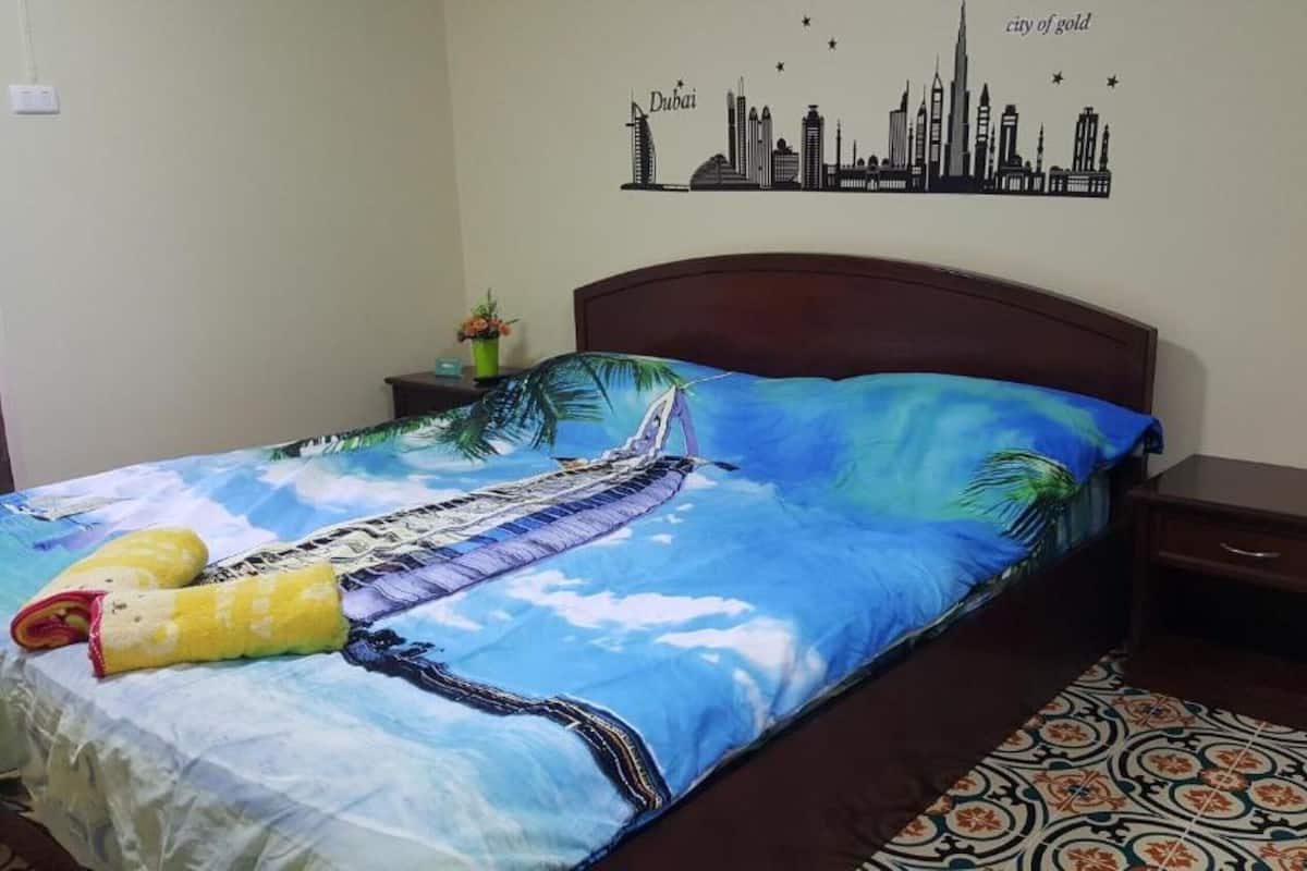 Ein Hotelzimmer mit einem Bett, das ein Stadt-Skyline-Wandbild, eine tropisch gestaltete Bettdecke und ein dekoratives Kissen zeigt.