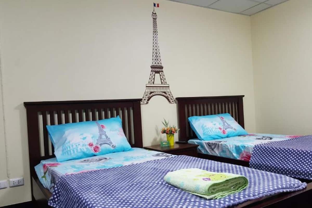 Ein Hotelzimmer mit zwei Betten, jedes mit einer blau-weißen Punkte-Bettdecke und Kissen mit Eiffelturm-Motiv.