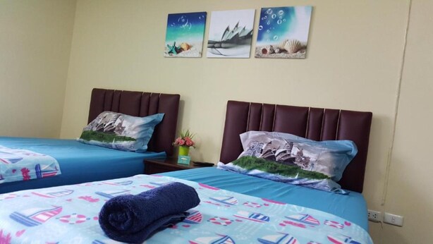 A hotel room with two beds, each with a blue bedspread and matching pillows. There are three wall art pieces above the beds, depicting nautical scenes.