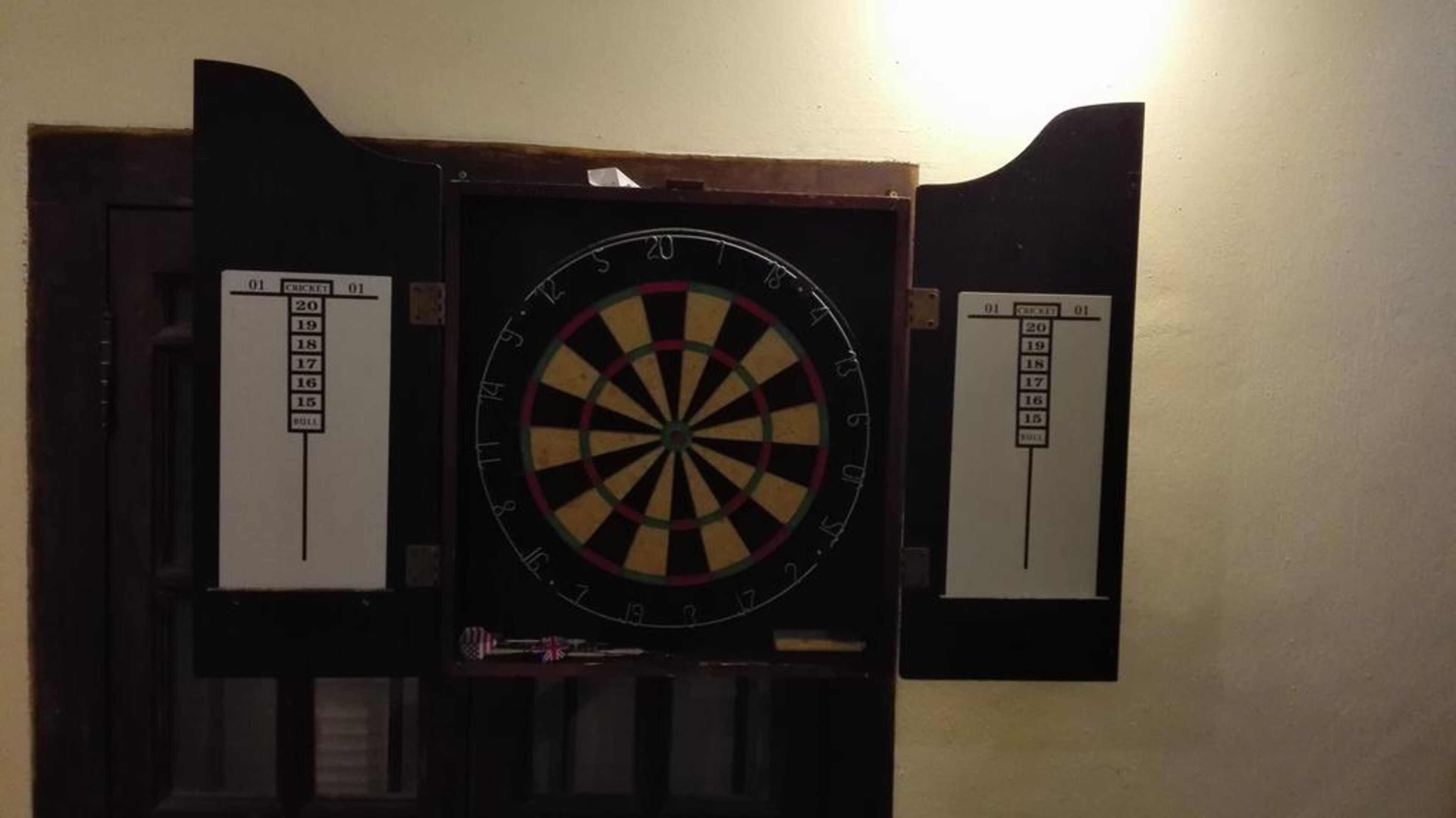 Une cible de fléchettes fixée au mur, avec des tableaux de pointage de chaque côté.
