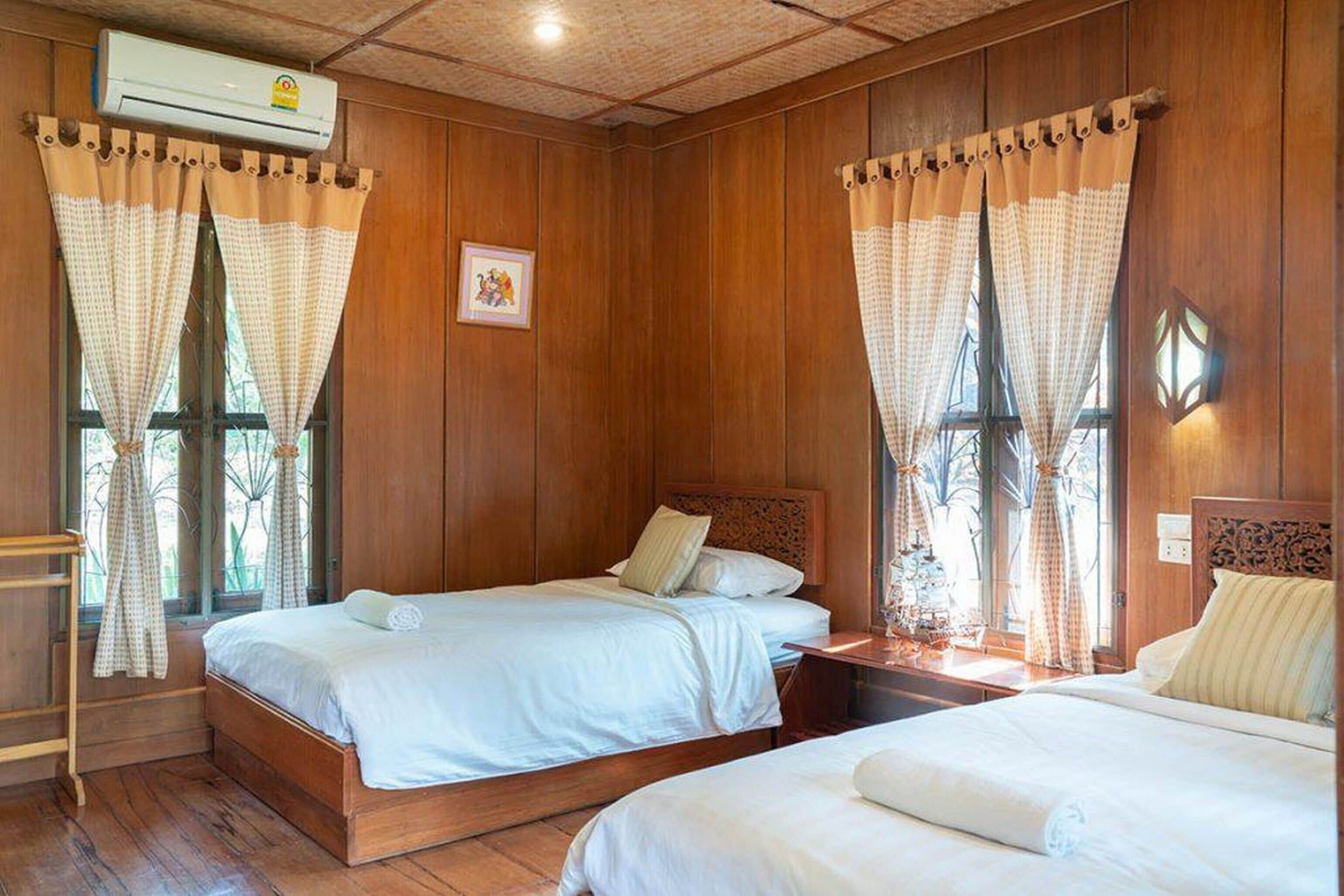 Una habitación con dos camas de madera, un armario de madera y una ventana con cortinas.