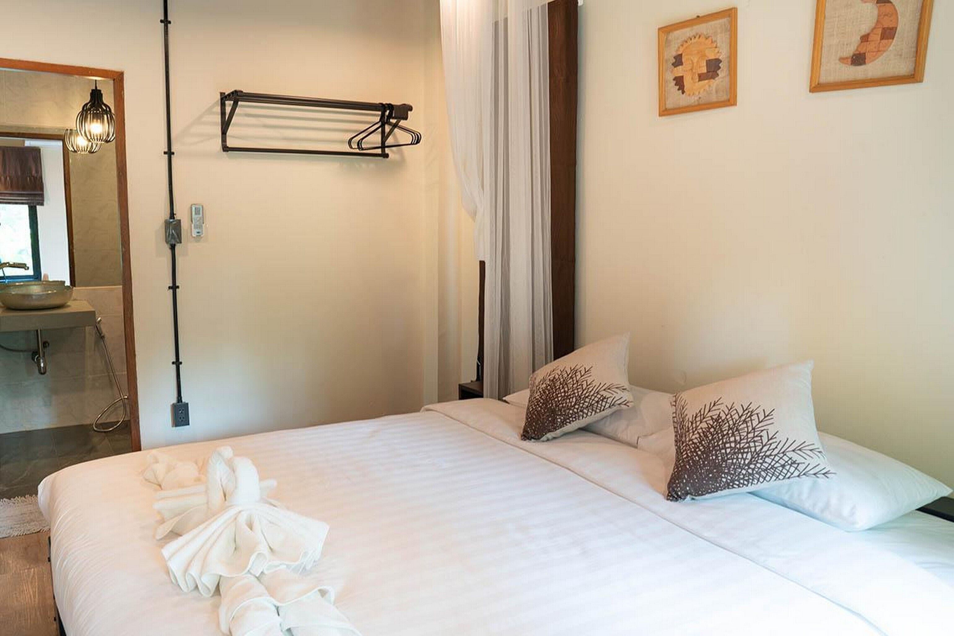 Habitación de hotel con una cama, dos almohadas, una toalla sobre la cama, un perchero para toallas, un lavamanos y un espejo.