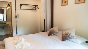 Habitación de hotel con una cama, dos almohadas, una toalla sobre la cama, un perchero para toallas, un lavamanos y un espejo.