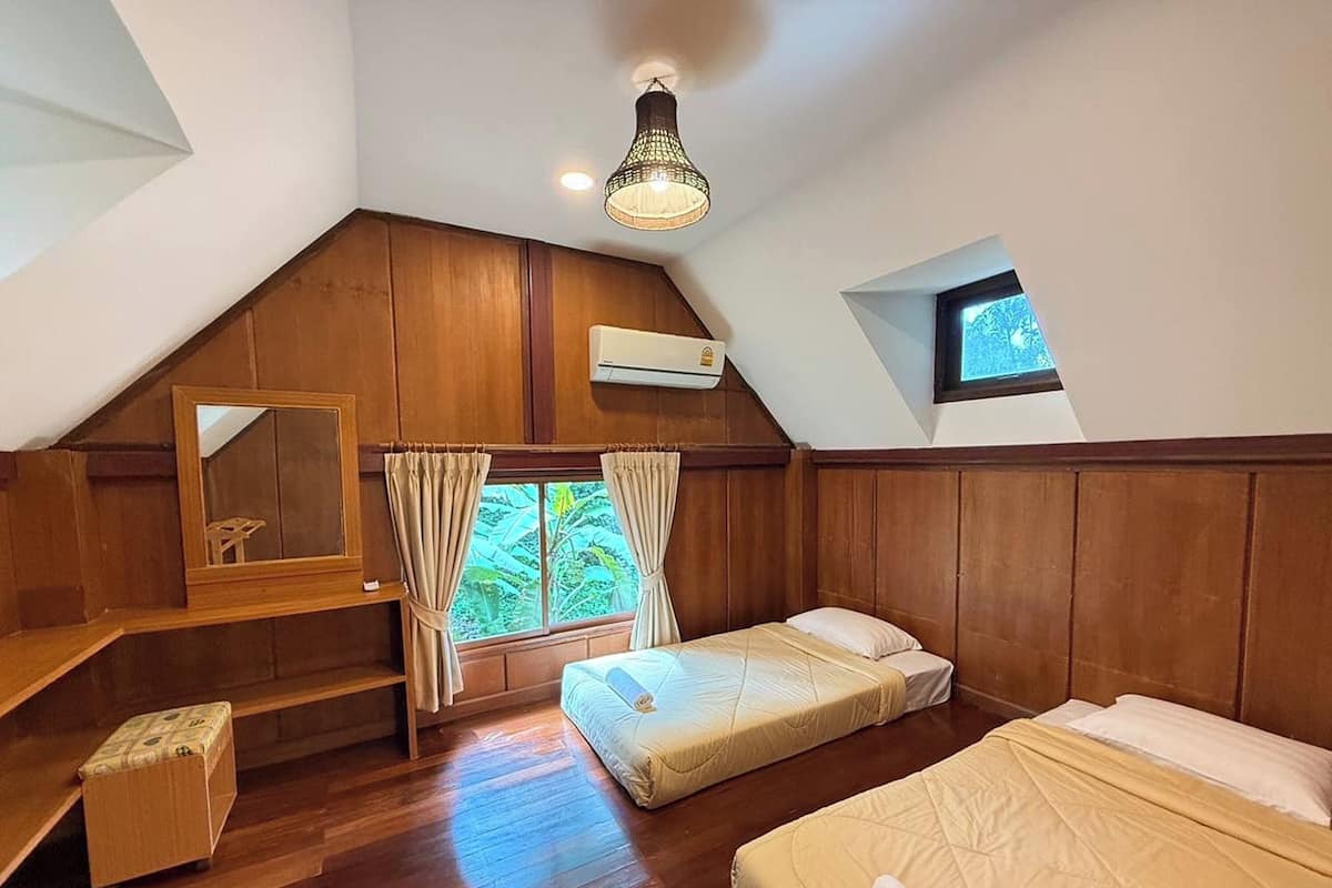 A cozy room with a sloped ceiling, wooden walls, a bed, a small desk, and a window with curtains.