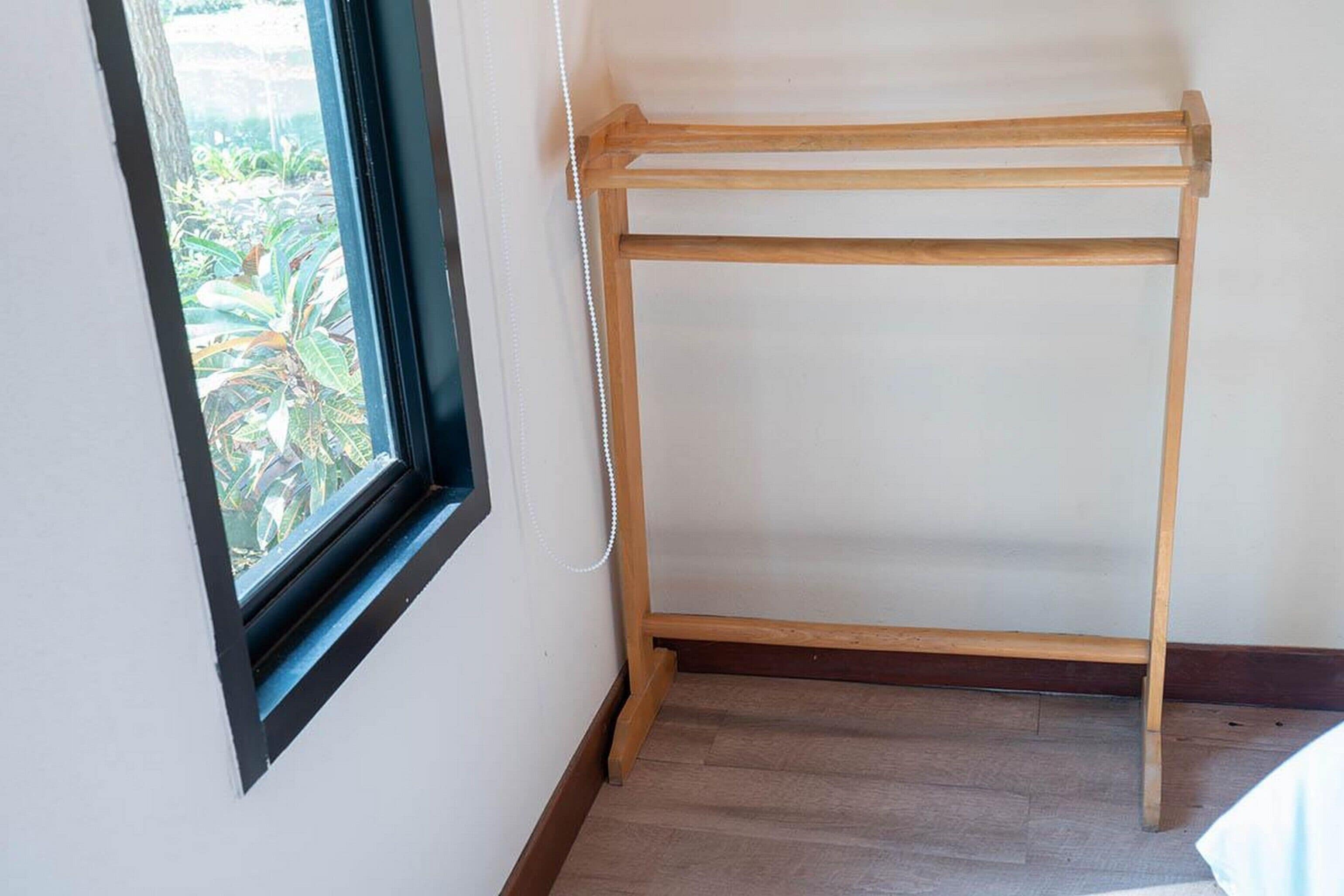 Un tendedero de madera apoyado contra una pared con una ventana.