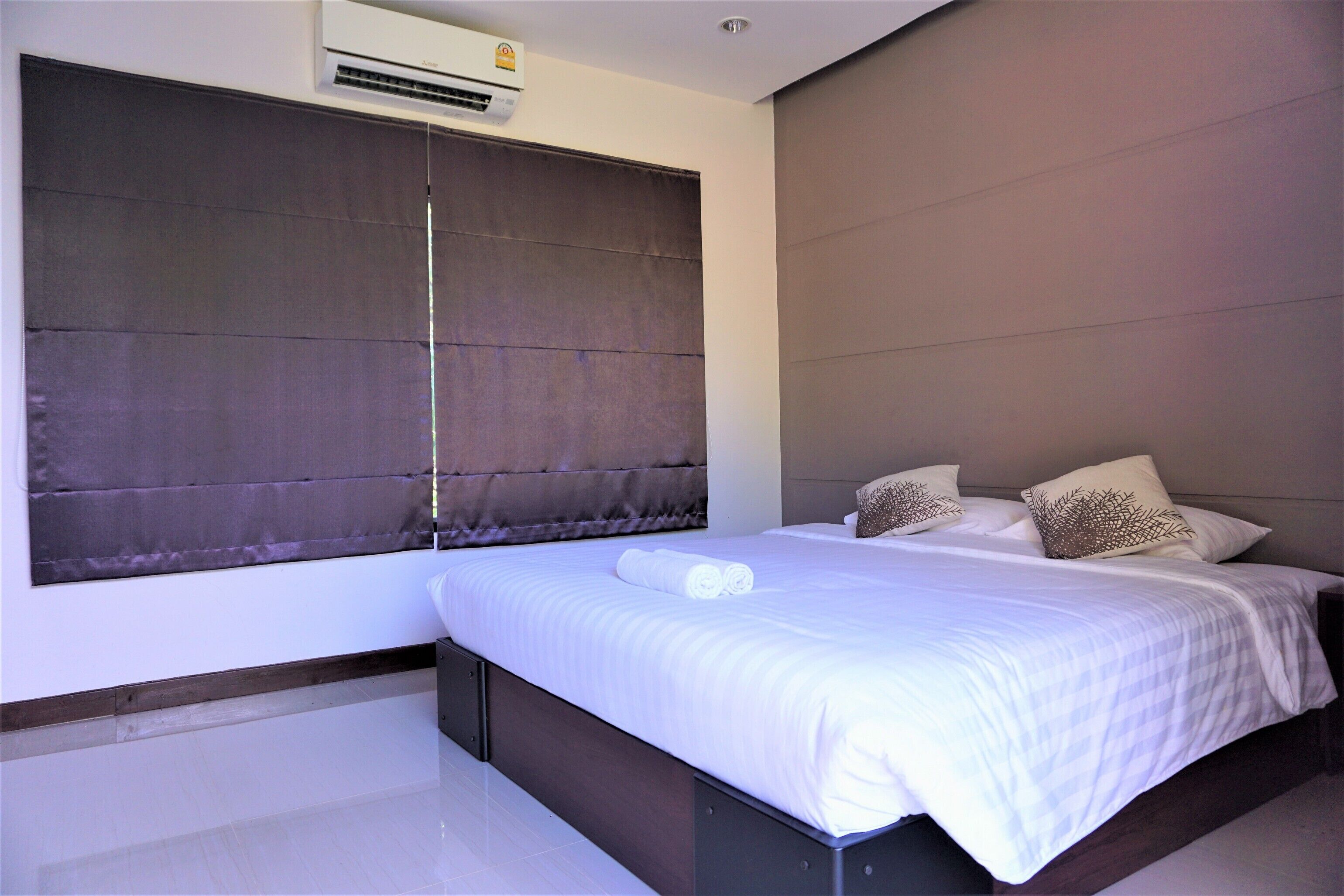 A modern bedroom with a large bed, a dark headboard, and a window with a blind.